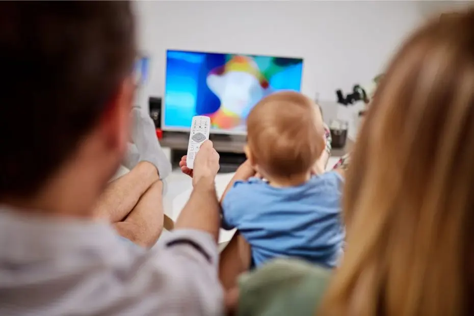 Bayi sedang menonton televisi (TV) bersama ibu dan ayah.